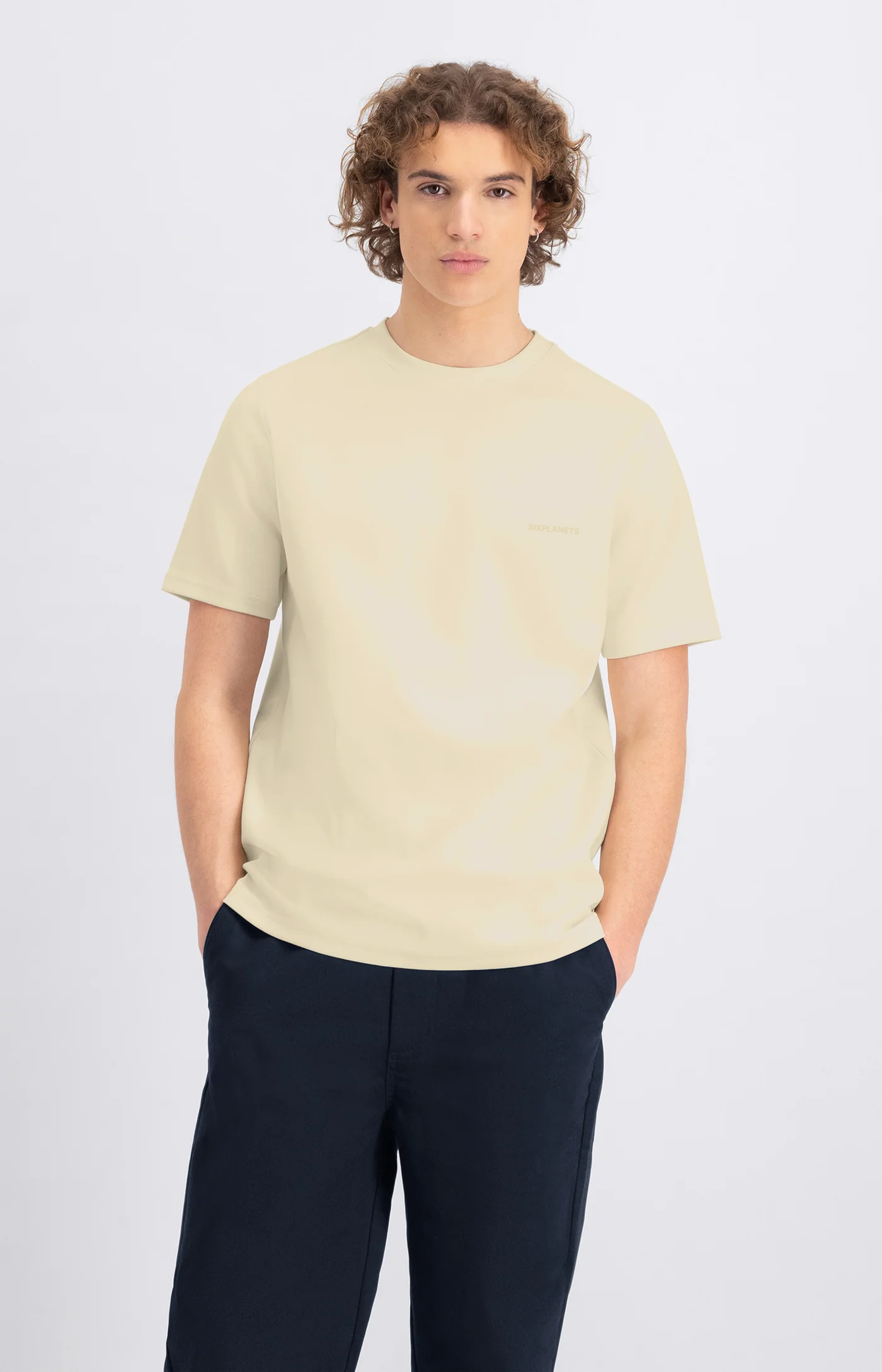 Man wearing a light-colored t-shirt and dark pants on a white background